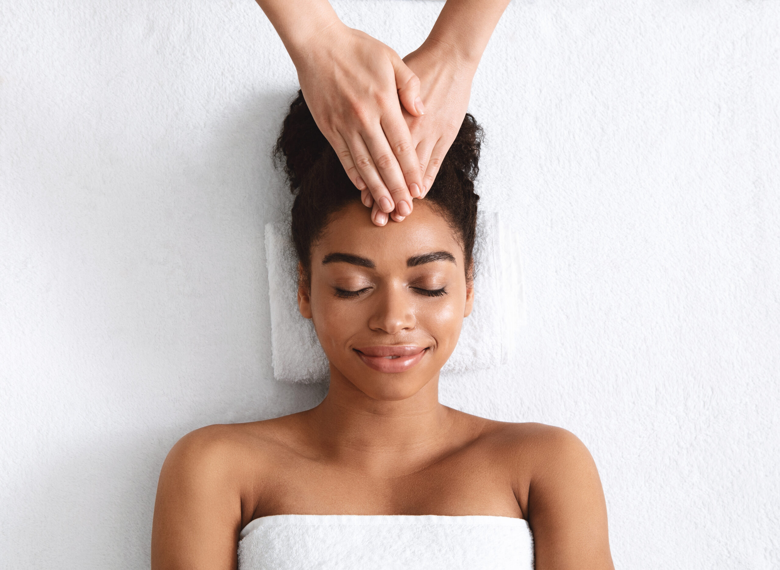 Therapist hands rubbing relaxed black woman forehead at spa, head massage benefits for headache, migraine, stress, top view